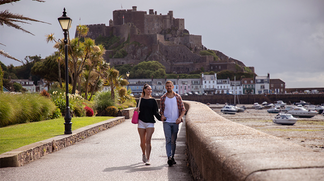 Couple walk hand in hand with Mont Orgueil Castle in the background